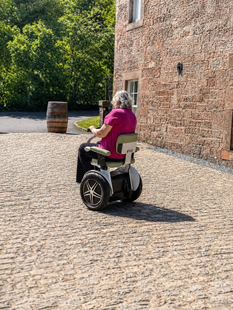 Person in magenta shirt riding a self-balancing scooter on a brick courtyard next to a stone building